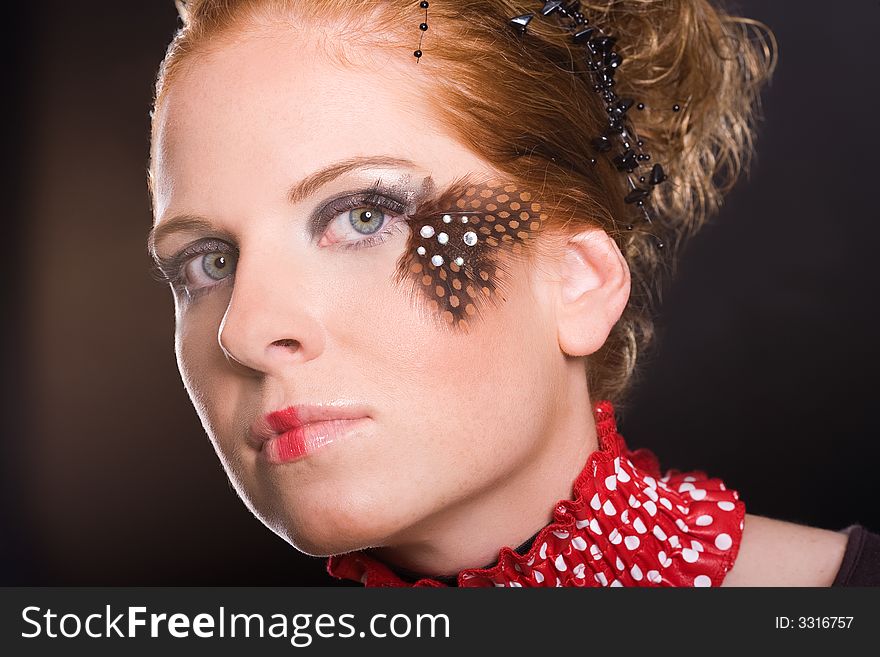 Attractive woman, unusual rogued, with feather on one eye and red-white vogue toby collar. Dark background. Attractive woman, unusual rogued, with feather on one eye and red-white vogue toby collar. Dark background.