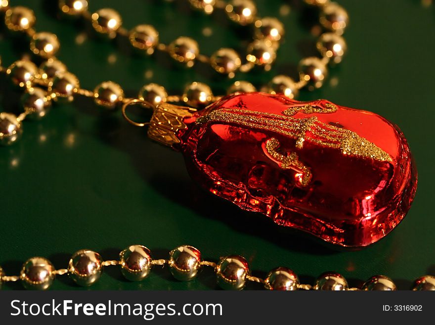 A piece of red and gold Christmas decoration shaped as a violin (cello, contrabass) with a string of gold beads, dark green background. A piece of red and gold Christmas decoration shaped as a violin (cello, contrabass) with a string of gold beads, dark green background.