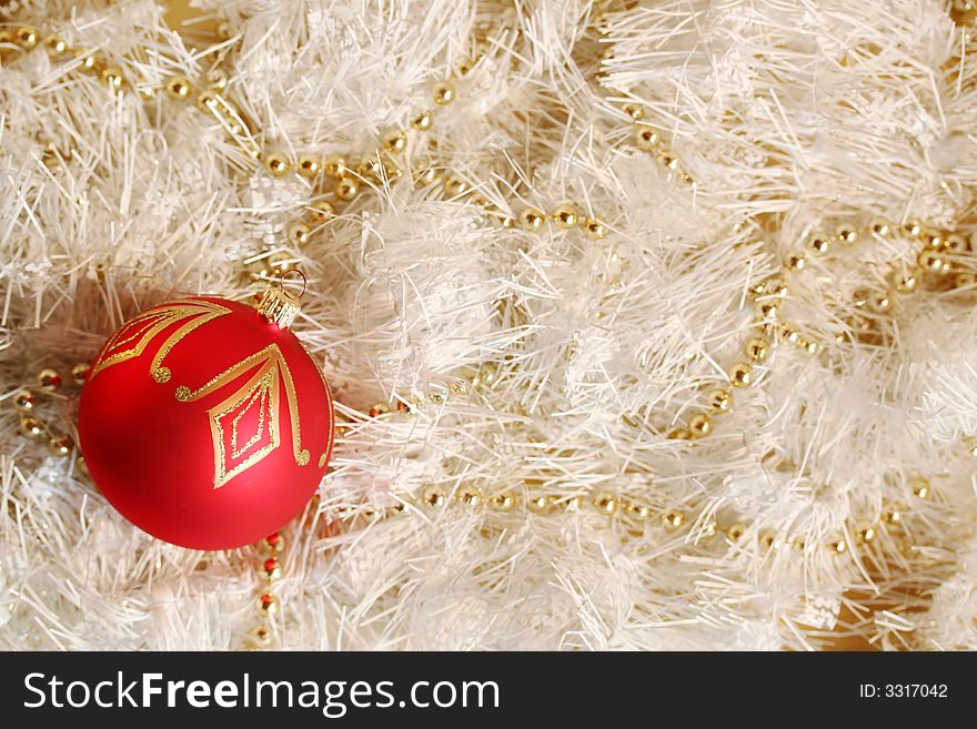 A red and gold piece of Christmas decoration lying in white and glittering strings and a string of gold beads. A red and gold piece of Christmas decoration lying in white and glittering strings and a string of gold beads.