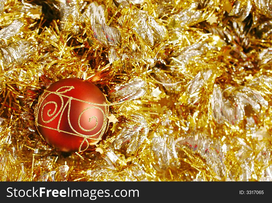A red and gold piece of Christmas decoration lying in rich gold and silver glittering strings. A red and gold piece of Christmas decoration lying in rich gold and silver glittering strings.