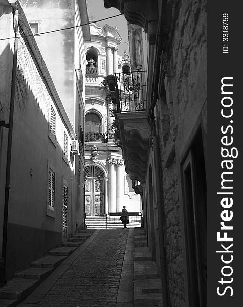 The view of a church and a woman through a little street in Scicli (Sicily). The view of a church and a woman through a little street in Scicli (Sicily)