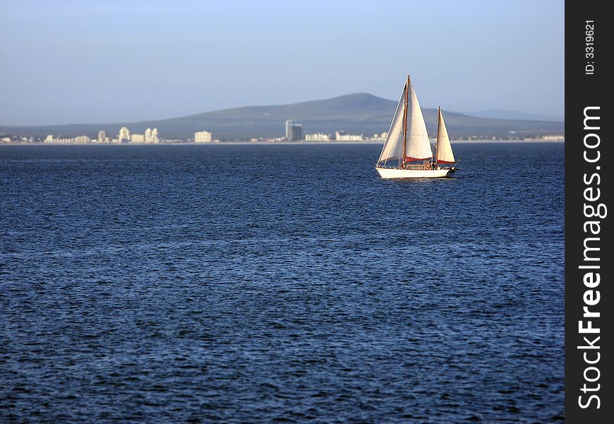 A single sailboat cruising across calm blue waters. A single sailboat cruising across calm blue waters