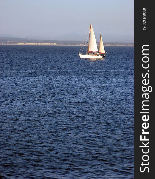 A single sailboat cruising across calm blue waters. A single sailboat cruising across calm blue waters