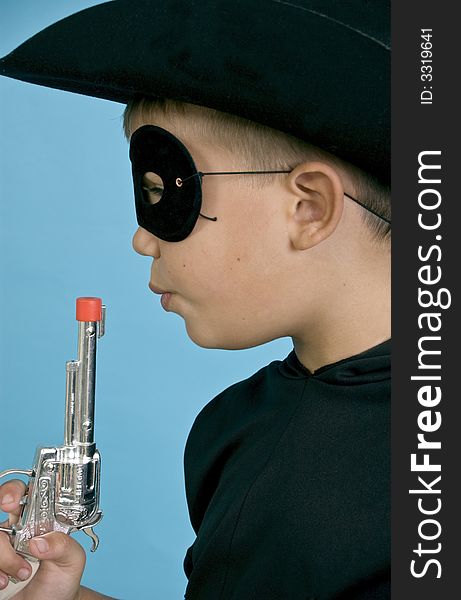 A child in a black cowboy hat and mask, blowing on the end of a toy gun, as if just discharged. A child in a black cowboy hat and mask, blowing on the end of a toy gun, as if just discharged.