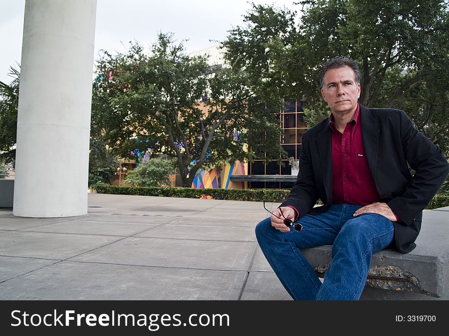 A man sitting on a stone bench with a colorful building in the background. A man sitting on a stone bench with a colorful building in the background.