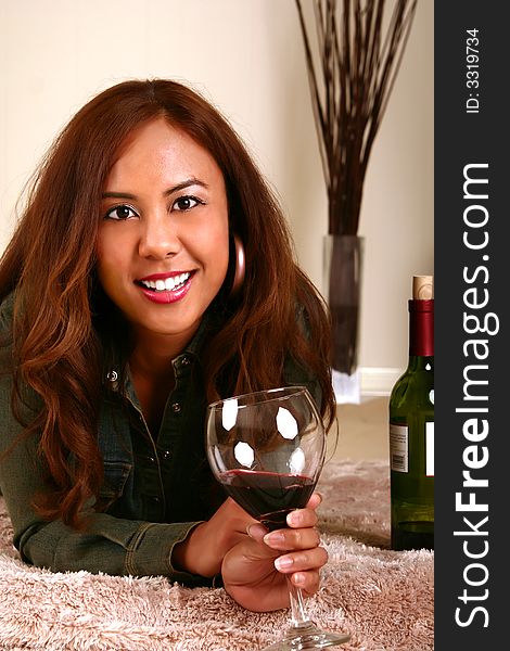 Shot of woman holding wine on and laying on her bed showing happy expression. Shot of woman holding wine on and laying on her bed showing happy expression