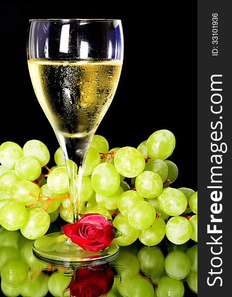 Wine glass and green grapes and a rose, reflection on objects in vertical position