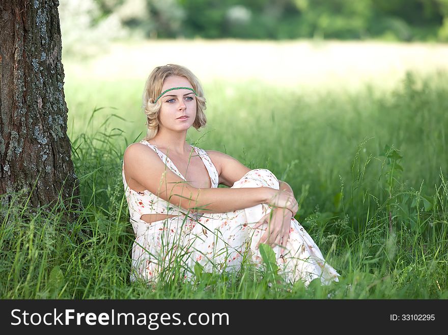 Beautiful girl in a long bright dress sitting in the grass near a tree trunk. Beautiful girl in a long bright dress sitting in the grass near a tree trunk