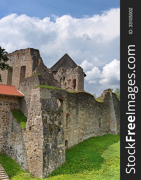 Ruins of the medieval castle on green grass under cloudy blue sky