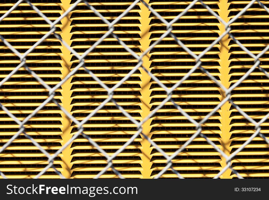 A chain link fence in front of a yellow metal panel for background or texture. A chain link fence in front of a yellow metal panel for background or texture.