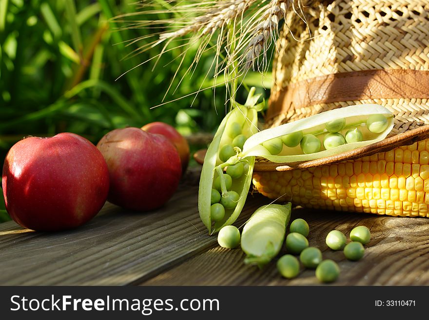 Green pot, corn, onions, apple  and straw hat.