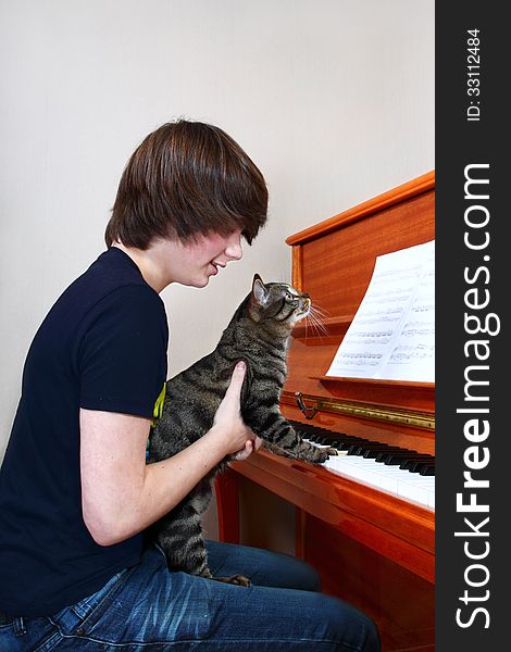 Teenage boy teaches a cat play piano. Teenage boy teaches a cat play piano