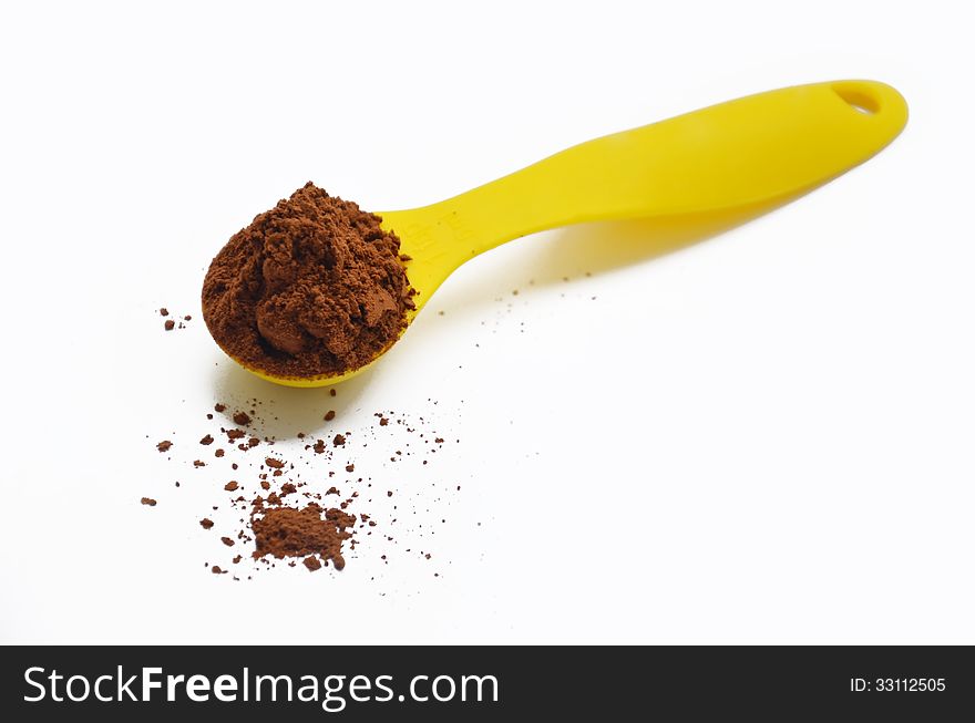 Metal spoon pointing towards the camera filled with chocolate powder which is spilling onto the surface below. Metal spoon pointing towards the camera filled with chocolate powder which is spilling onto the surface below