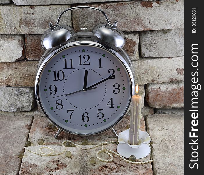 Old-fashioned clock with burning candle and decorations on stone background. Old-fashioned clock with burning candle and decorations on stone background