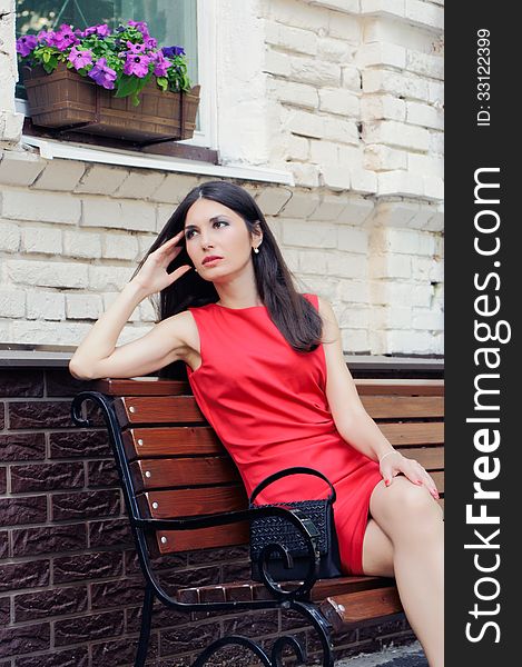 The elegant girl sits on a bench on the street