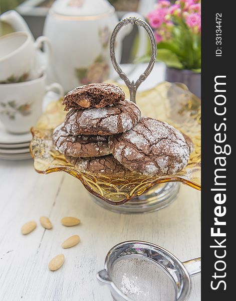 Chocolate and almond cookies with tea set and flowers in the background