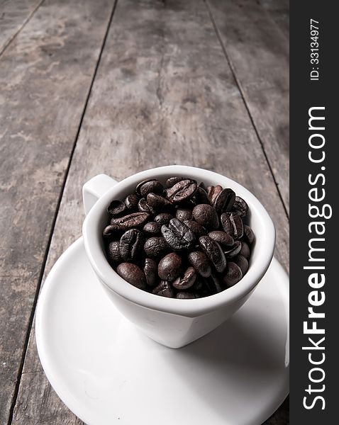 Coffee beans in white coffee cup on wooden background