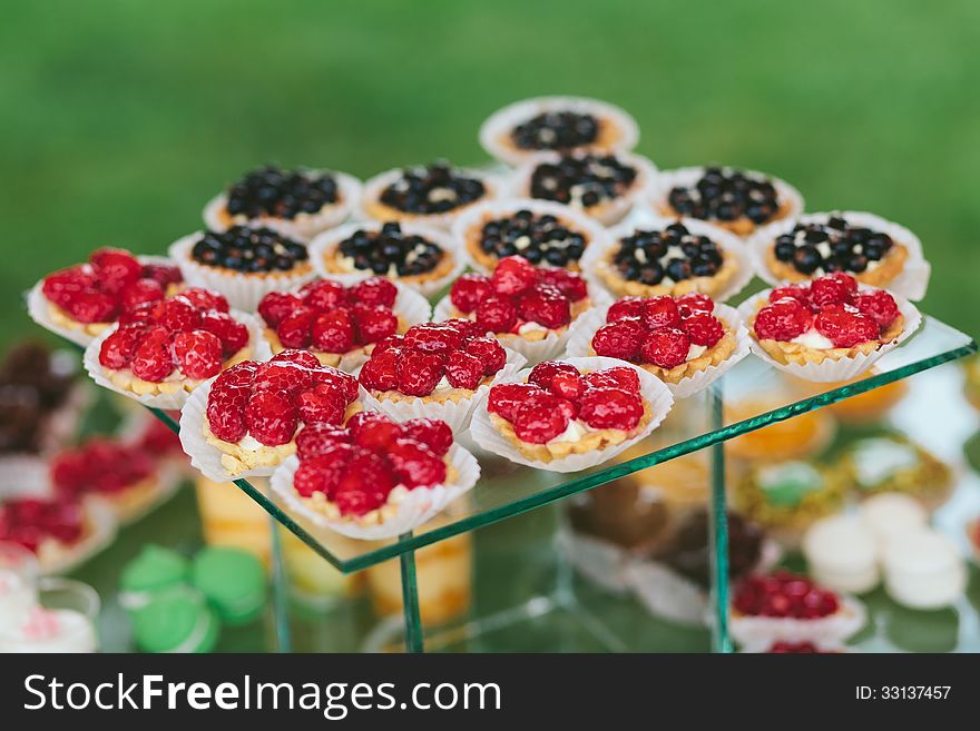 A bunch of fruits cupcakes sitting on glass table with green background. A bunch of fruits cupcakes sitting on glass table with green background.