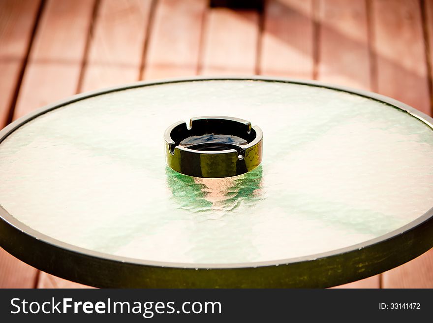 Empty ashtray stands in the middle of a round glass table