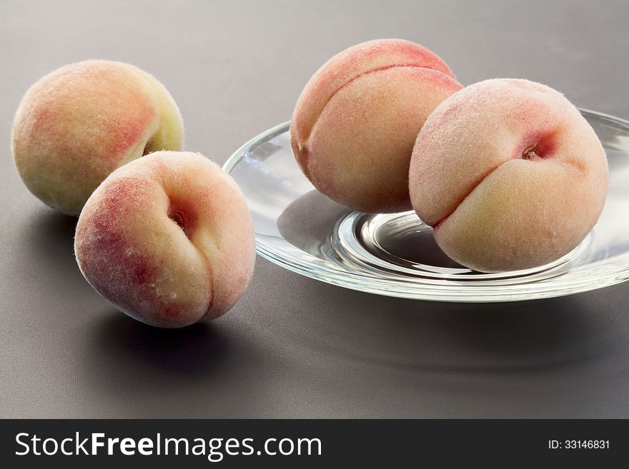 Goldish velvety ripe peaches on a glass saucer