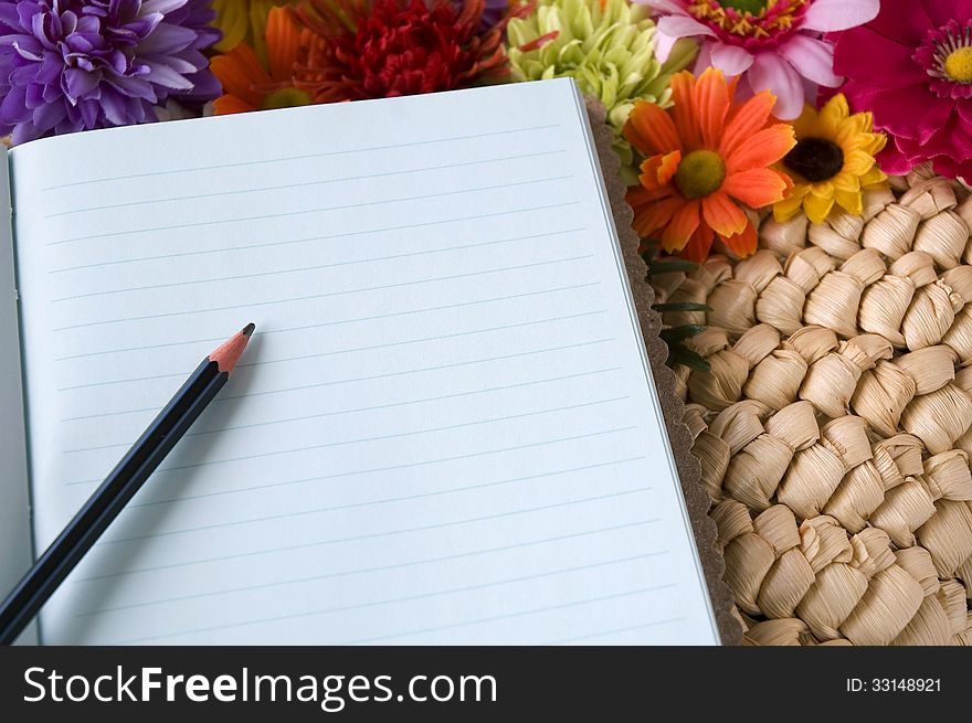 Pencil put on notebook with flowers blooming background