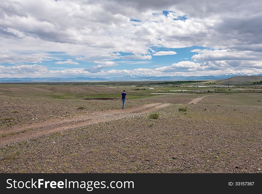 man goes along dirt road steppe sky