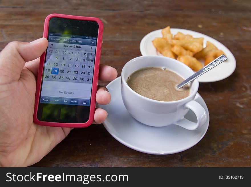 Hand holding phone with coffee cup on table in morning. Hand holding phone with coffee cup on table in morning
