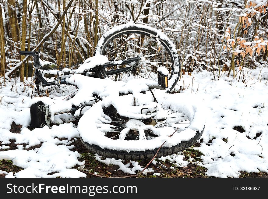 An abandoned bicycle is lying in the winter park. The lorn bike and all around are covered with light wet snow. An abandoned bicycle is lying in the winter park. The lorn bike and all around are covered with light wet snow.