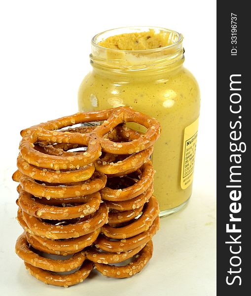 A stack of pretzels with a jar of mustard.