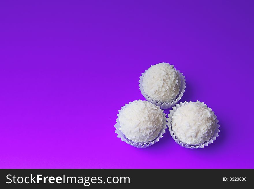 Appetizing candies with a nut and coconut are sparse on a violet background