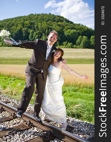 Bridal couple on rails, being in the nature. Great azure sky. Great summer! He balances on one foot on the rail.. They have fun. Bridal couple on rails, being in the nature. Great azure sky. Great summer! He balances on one foot on the rail.. They have fun.