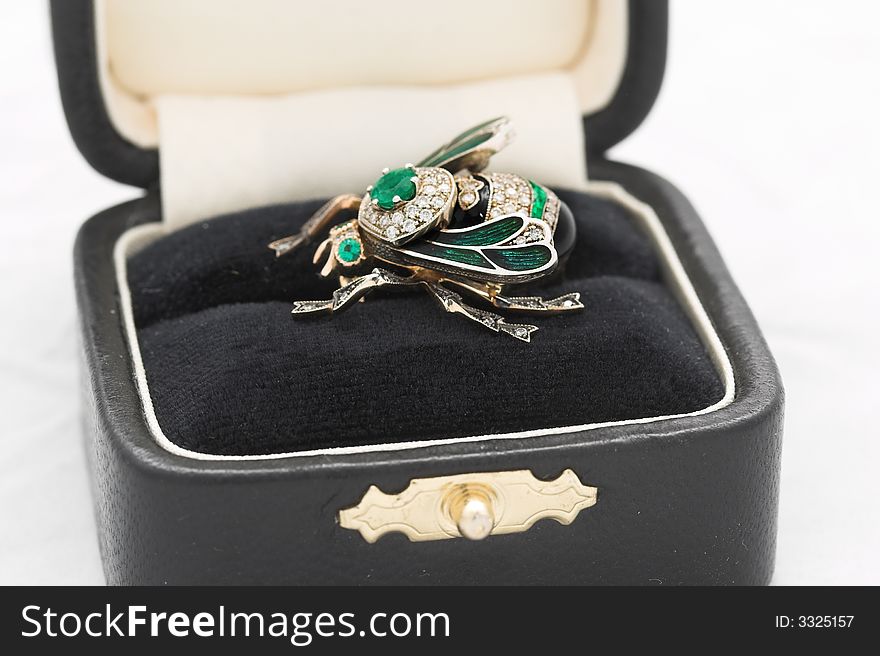 Jewelry from gold, emeralds, brilliants and platinum in the form of a bee in a small box on a white background. Jewelry from gold, emeralds, brilliants and platinum in the form of a bee in a small box on a white background