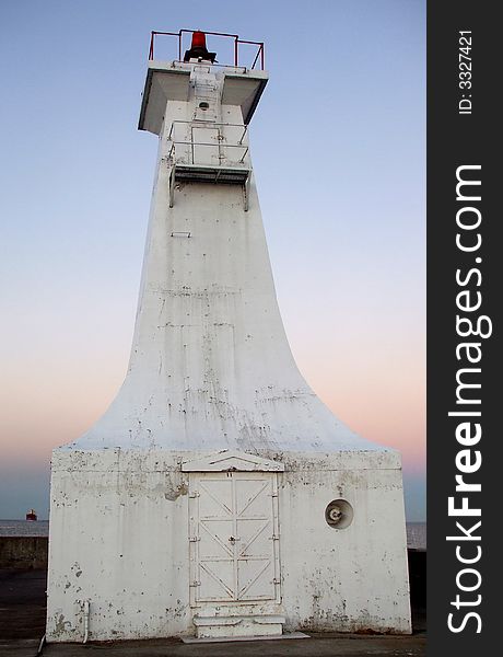 A white lighthouse on the pier at sunset.