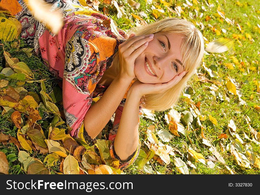 Blond cheerful girl lying on autumn leaves