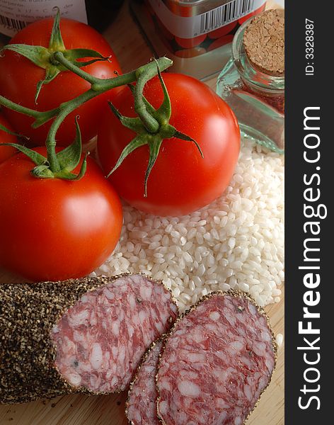 Piled up ingredients to make a risotto or paella, tin and jar of spices, tomatoes, rice and salami. Piled up ingredients to make a risotto or paella, tin and jar of spices, tomatoes, rice and salami