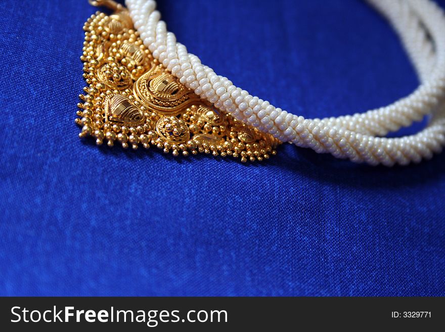 Gold and pearl jewelery necklace on blue background. Gold and pearl jewelery necklace on blue background.