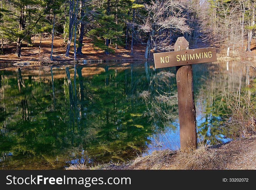 Rustic wooden no swimming sign shown at a mountain lake in autumn, reminiscent of a cross.