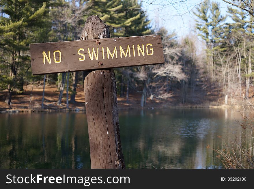 Rustic wooden no swimming sign shown at a mountain lake in autumn, reminiscent of a cross.