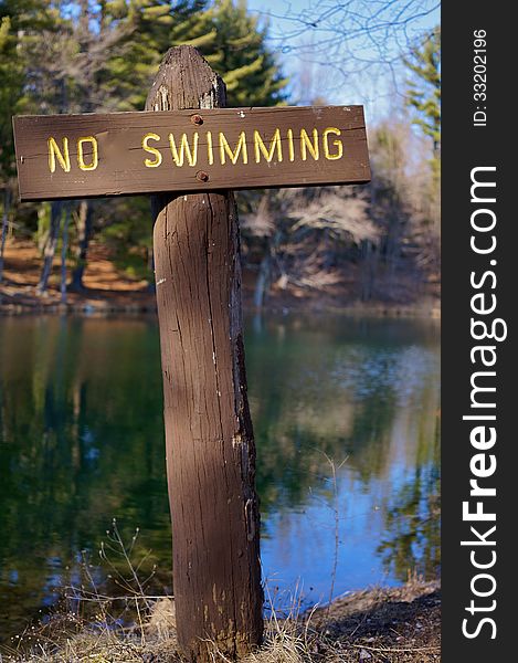 Rustic wooden no swimming sign shown at a mountain lake in autumn, reminiscent of a cross.