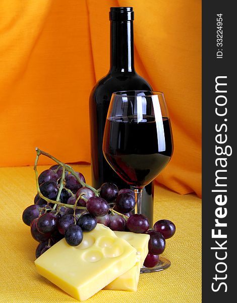 Cheese and a glass of red wine with grapes on black background created with brightly colored fabrics. Cheese and a glass of red wine with grapes on black background created with brightly colored fabrics