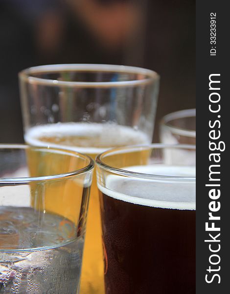 Icy glasses of light and dark beers on table at outdoor eatery.