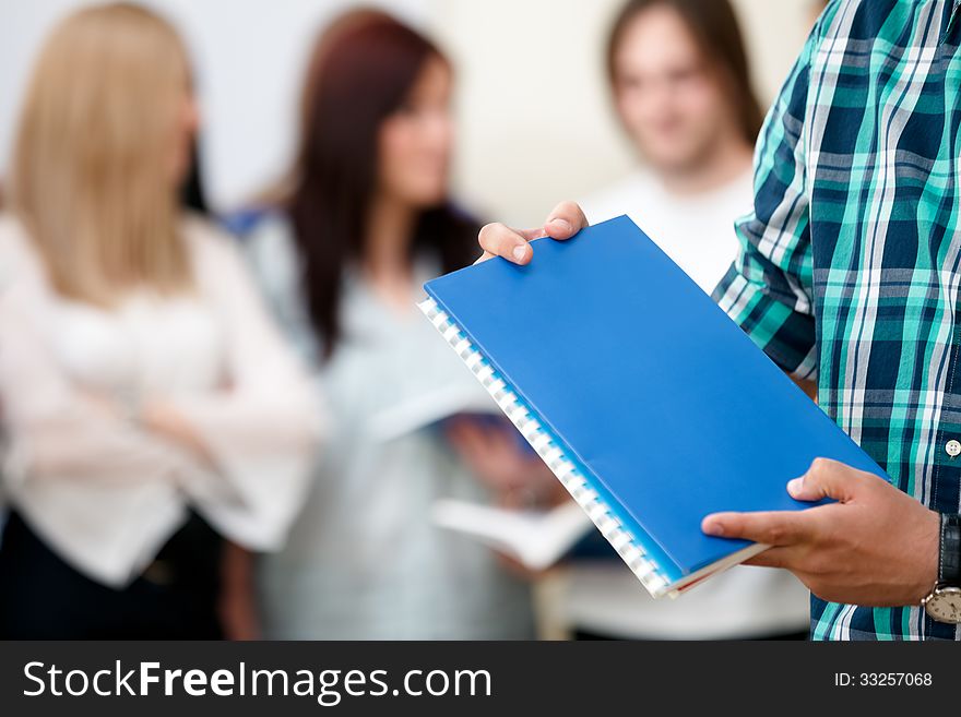 Student holding notebooks with a group of students behind. Student holding notebooks with a group of students behind