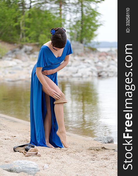 Beautiful younge girl in a blue dress stockings strips on the lake in the woods. Beautiful younge girl in a blue dress stockings strips on the lake in the woods