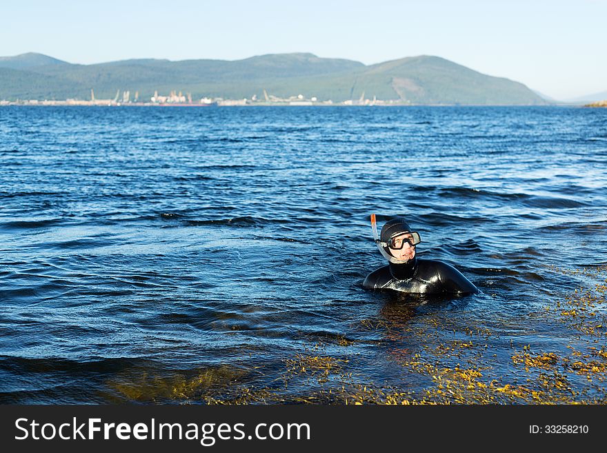 Underwater hunter in a wetsuit in the water on the background of the port with cranes in the background. Underwater hunter in a wetsuit in the water on the background of the port with cranes in the background