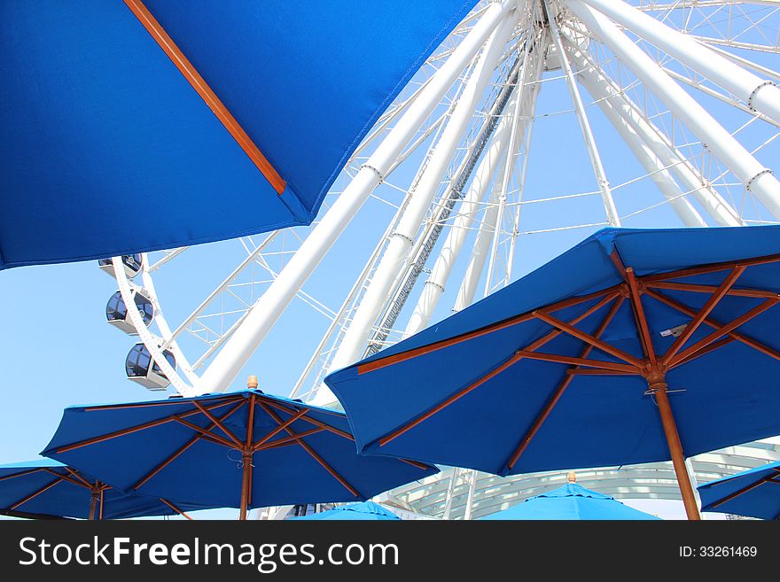 Partial view of large Ferris wheel in Seattle, Washington with blue restaurant umbrellas. Partial view of large Ferris wheel in Seattle, Washington with blue restaurant umbrellas.