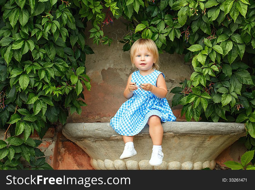 Little blonde girl on a background of green grape leaves. Little blonde girl on a background of green grape leaves