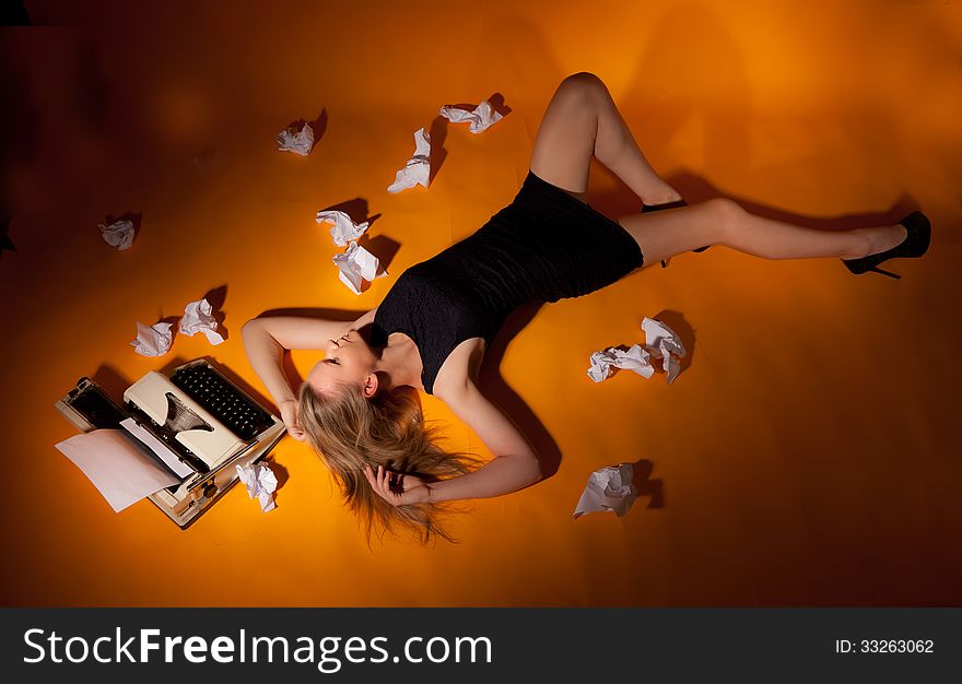 Beautiful girl lies at the typewriter, surrounded by crumpled scraps of paper. Beautiful girl lies at the typewriter, surrounded by crumpled scraps of paper.