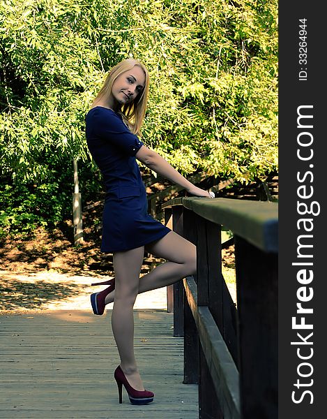 A girl in a short dress and high heels standing on a wooden bridge