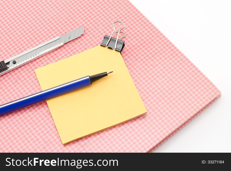 Red notebook with post it and bulldog clip blue pen cutter isolated on white background