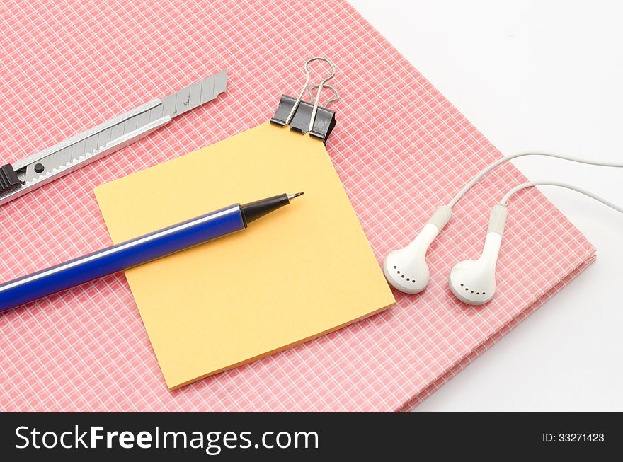 Red notebook with post it and bulldog clip blue pen cutter ear phone isolated on white background